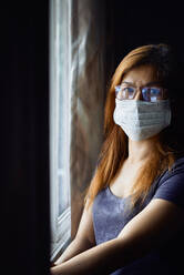 Woman in mask at the window during COVID-19 pandemic - CAVF83860