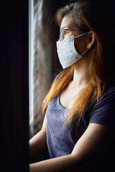 Woman in mask at the window during COVID-19 pandemic - CAVF83861