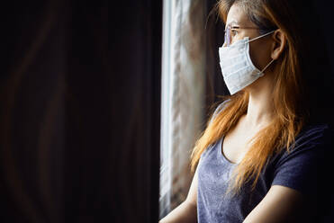 Woman in mask at the window during COVID-19 pandemic - CAVF83862