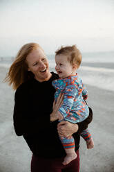 Junge Mutter und gesundes pummeliges Kind lächeln bei einem Strandspaziergang - CAVF83866