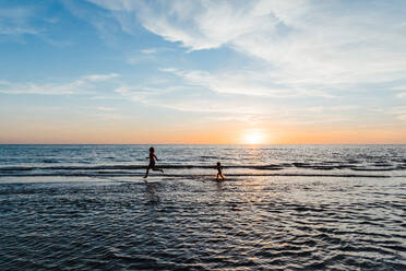 Frau und Kind laufen im seichten Wasser eines Strandes in Florida bei Sonnenuntergang - CAVF83869