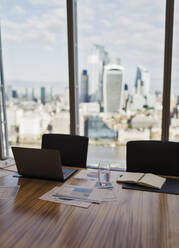 Laptop und Papierkram auf einem Konferenzraumtisch mit Blick auf die Stadt - CAIF27779