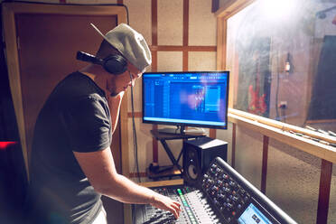 Male music producer working at sound board in recording studio - CAIF27809