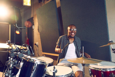 Glücklicher männlicher Musiker spielt Schlagzeug im Aufnahmestudio - CAIF27847