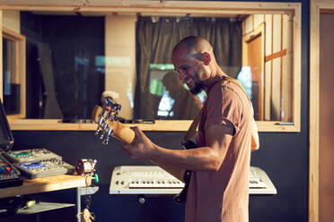 Glücklicher männlicher Musiker spielt Gitarre im Aufnahmestudio - CAIF27895