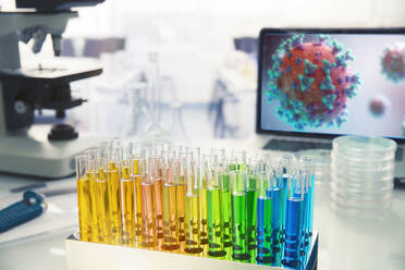 Mehrfarbige Fläschchen auf dem Labortisch neben dem Coronavirus auf dem Bildschirm - CAIF27918