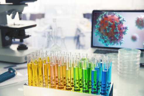 Multicolor vials on laboratory table next to coronavirus on screen - CAIF27918