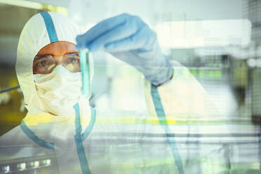 Male scientist in clean suit studying vial in laboratory - CAIF27933