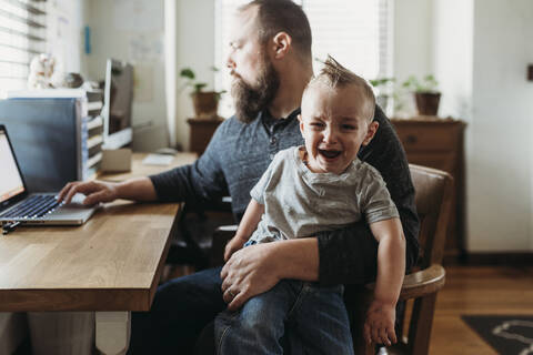 Father trying to work from home with toddler screaming in his lap stock photo