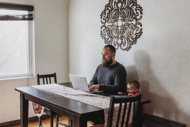 Wide view of father trying to work from home with toddler standing - CAVF84192