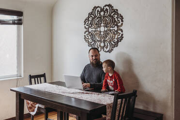 Wide view of father trying to work from home with toddler standing - CAVF84194
