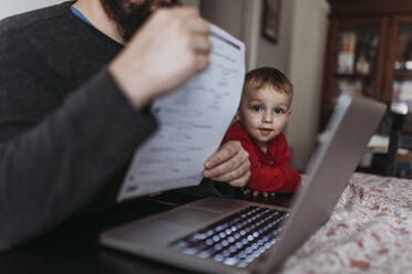 Nahaufnahme eines kleinen Sohnes, der auf den Computer seines Vaters schaut, während dieser zu Hause arbeitet - CAVF84197