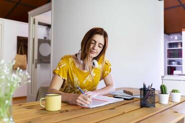Junge Frau schreibt während der Ausgangssperre in ein Buch und arbeitet zu Hause - AFVF06471