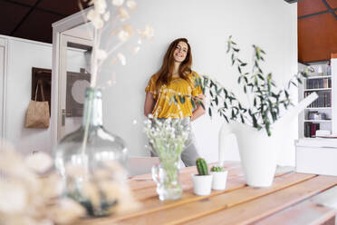 Smiling young woman standing against wall at home during curfew - AFVF06484