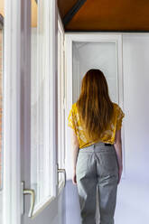 Junge Frau mit langen Haaren steht am Fenster zu Hause - AFVF06489
