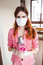 Female reporter wearing mask holding microphone while standing at home - LJF01555