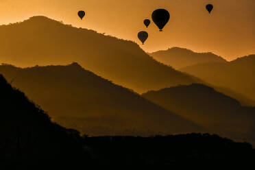 Indonesien, West Nusa Tenggara, Silhouetten von Heißluftballons, die in der stimmungsvollen Abenddämmerung über die Insel Sumbawa fliegen - KNTF04653