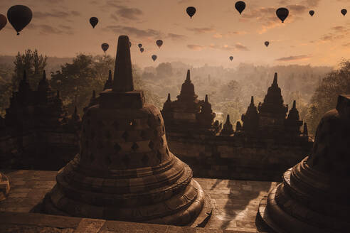 Indonesien, Zentral-Java, Magelang, Silhouetten von Heißluftballons, die in der Abenddämmerung über den Borobudur-Tempel fliegen - KNTF04658