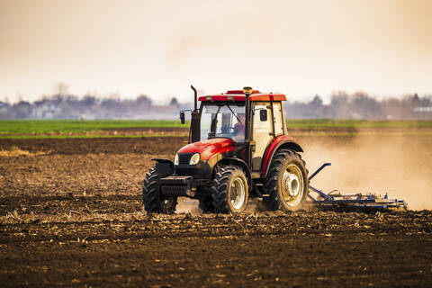 Landwirt im Traktor pflügt Bauernhof gegen den Himmel, lizenzfreies Stockfoto