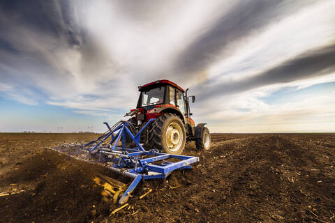Landwirt im Traktor pflügt landwirtschaftliche Flächen gegen bewölkten Himmel, lizenzfreies Stockfoto