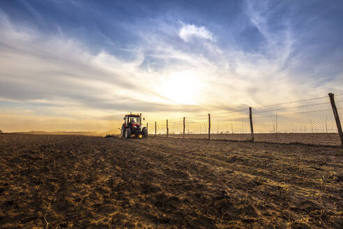 Landwirt im Traktor pflügt landwirtschaftliche Flächen gegen bewölkten Himmel - NOF00100