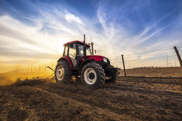 Mann in Traktor pflügt landwirtschaftliche Flächen gegen bewölkten Himmel - NOF00101