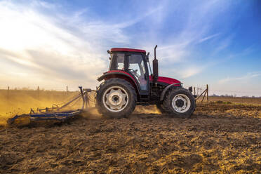 Mann in Traktor pflügt landwirtschaftliches Feld gegen bewölkten Himmel - NOF00102
