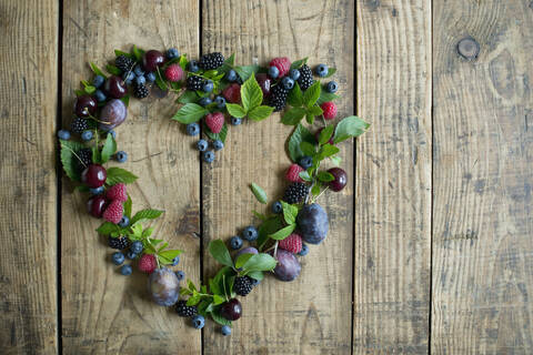 Heart shape made of fresh berries, plums and cherries on wood stock photo