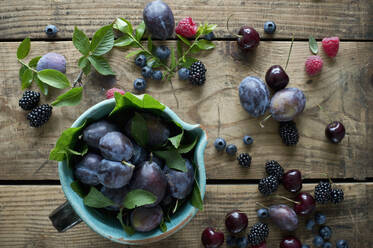 Jug and fresh berries, plums and cherries on wooden surface - ASF06625