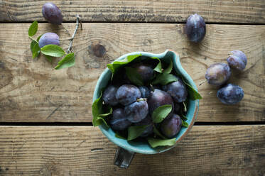 Jug of fresh plums standing on wooden surface - ASF06626