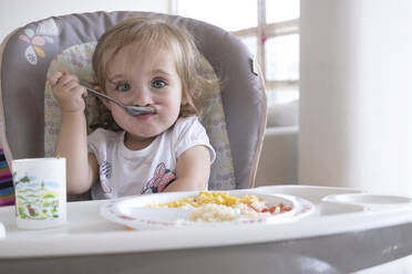 Kleines Mädchen isst allein auf einem Stuhl am Tisch. - CAVF84376