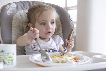 Kleines Mädchen isst allein auf einem Stuhl am Tisch. - CAVF84377