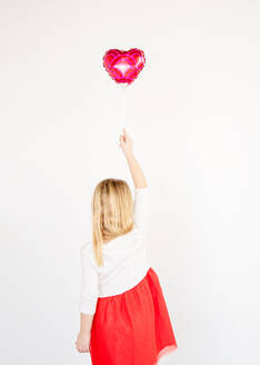 Rückansicht kleines blondes Mädchen in rotem Tutu hält roten Herzballon - CAVF84389