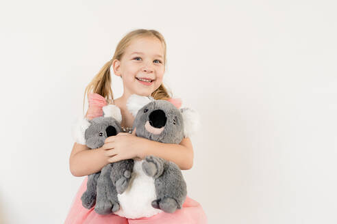 Niedliches blondes kleines Mädchen umarmt Koala-Stofftiere im Haus - CAVF84391