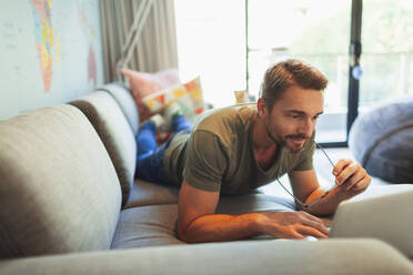 Man relaxing, laying on sofa using laptop - HOXF06271