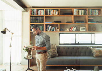 Man reading book in modern living room - HOXF06274