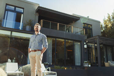 Smiling, confident man on sunny, luxury patio - HOXF06280