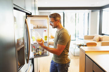 Mann hält Orangensaft am offenen Kühlschrank in der Küche - HOXF06310