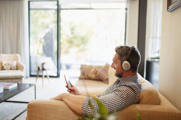 Mann mit Kopfhörern und mp3-Player beim Musikhören zu Hause - HOXF06320