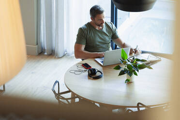Man using laptop, working from home at dining table - HOXF06321