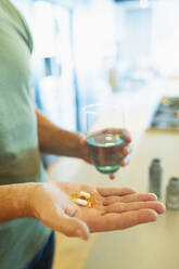 Close up man taking vitamins and supplements with glass of water - HOXF06325