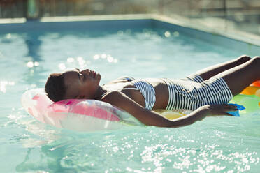 Serene young woman laying on inflatable raft in sunny swimming pool - HOXF06333
