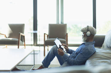 Mann entspannt sich, hört Musik mit Kopfhörern und digitalem Tablet im Wohnzimmer - HOXF06334