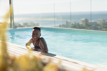 Glückliche junge Frau im sonnigen, luxuriösen Schwimmbad - HOXF06349