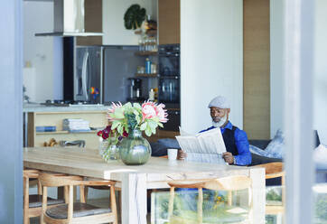 Mann liest Zeitung und trinkt Kaffee am Esstisch - HOXF06350