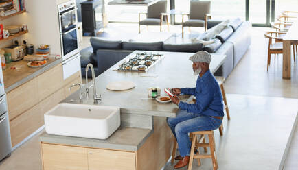 Man eating breakfast and using smart phone in modern kitchen - HOXF06373