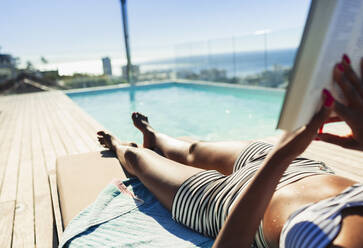 Young woman sunbathing, reading book at sunny poolside - HOXF06384