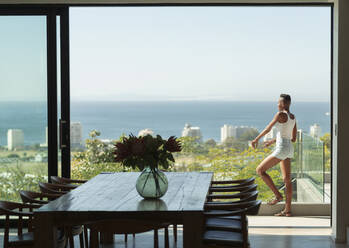 Junge Frau steht auf einem modernen Balkon mit sonnigem Meerblick - HOXF06403