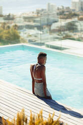 Serene young woman at sunny rooftop swimming pool - HOXF06409