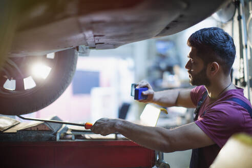 Männlicher Mechaniker arbeitet unter einem Auto in einer Autowerkstatt - HOXF06410